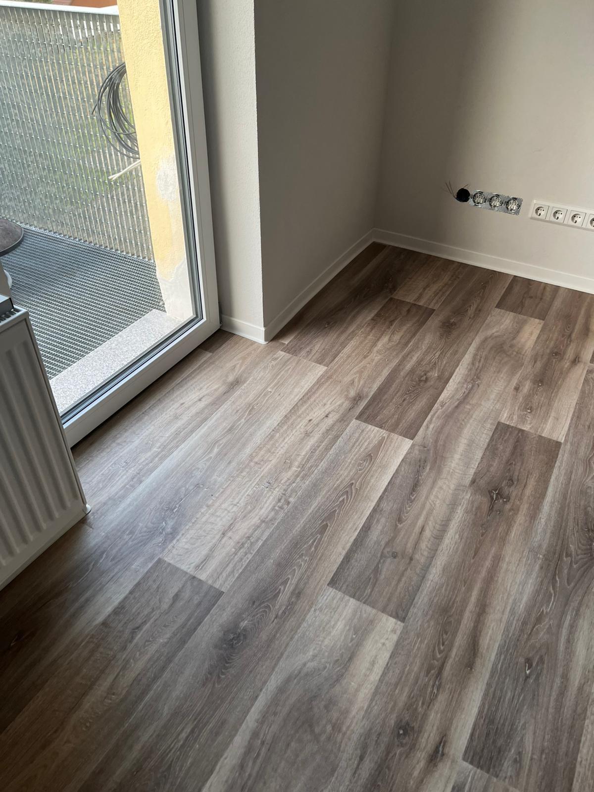 PVC-Boden im Wohnzimmer in Freiberg, verlegt bis an die Terrassentür mit weißen Sockelleisten